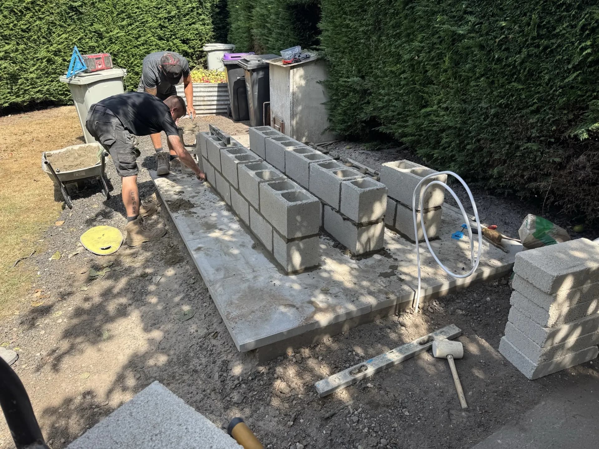 Two oil tank engineers constructing a raised blockwork plinth on a paved foundation