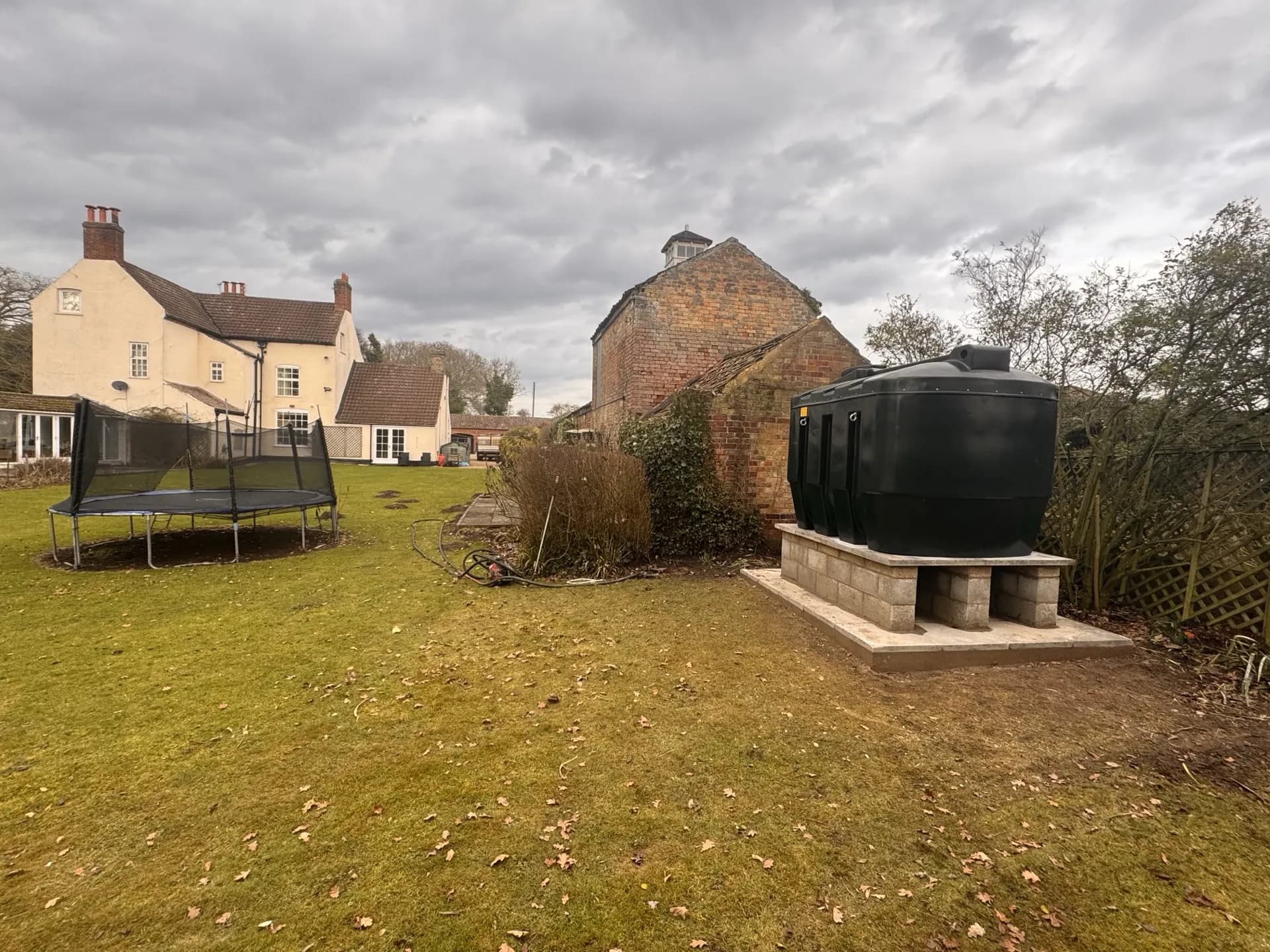 Wide view of a completed black bunded oil tank installation in a garden
