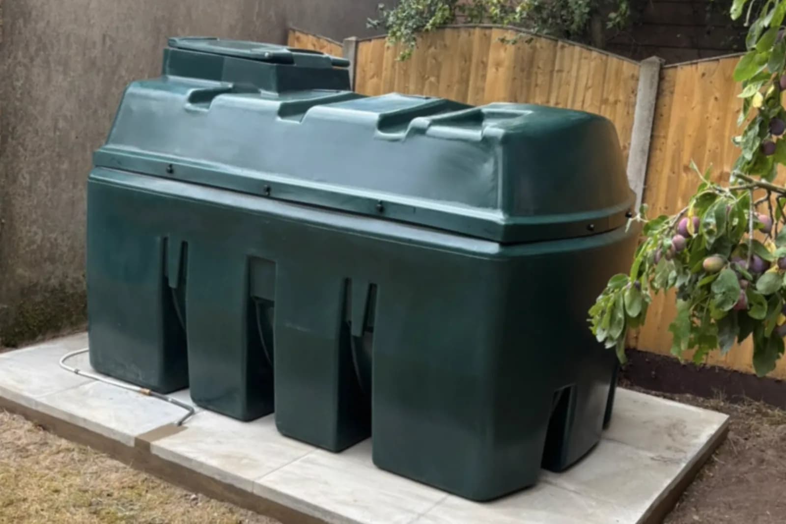 A new green bunded replacement oil tank installed on a level paving-slab base in a garden